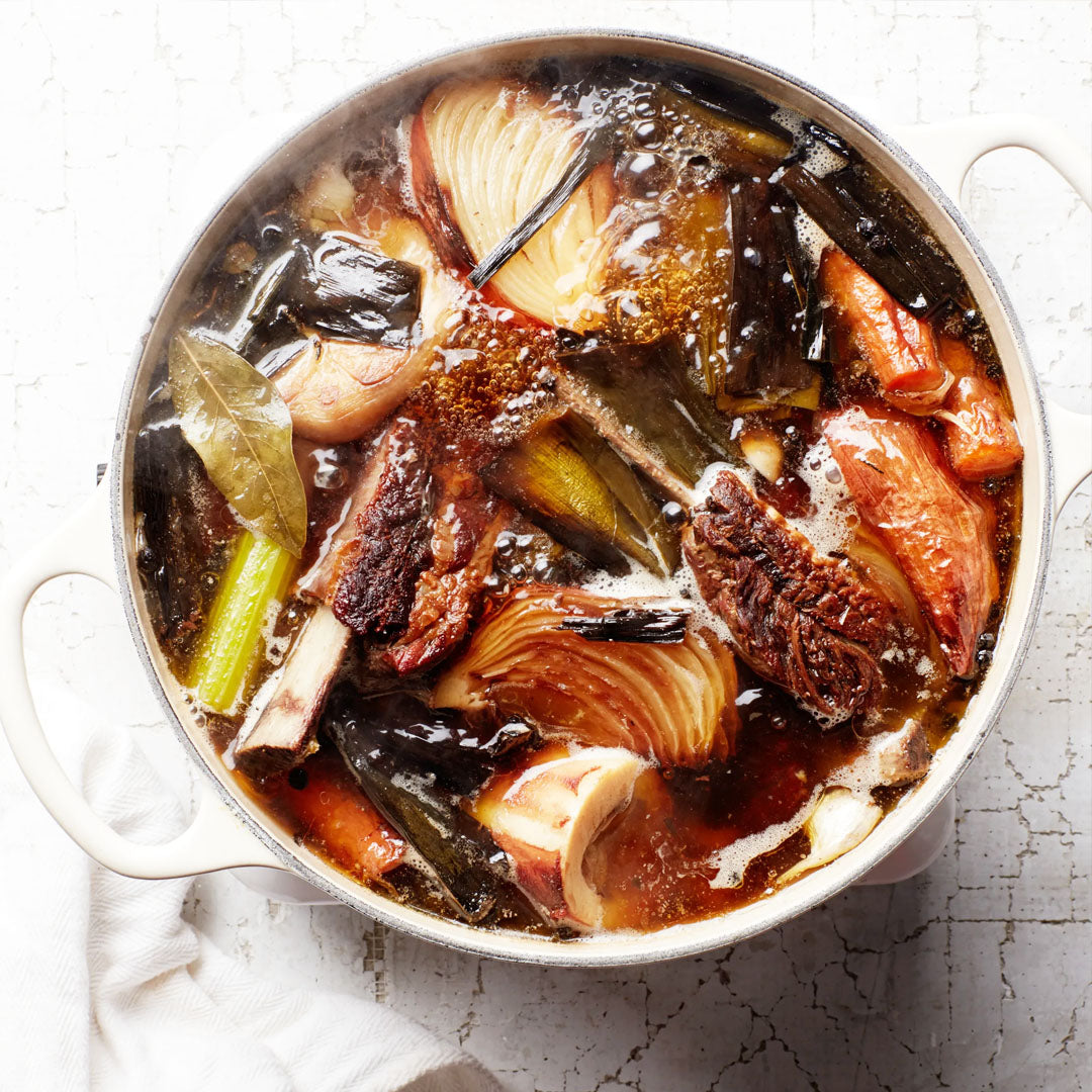Bone broth stew with vegetables in a pot on a textured surface