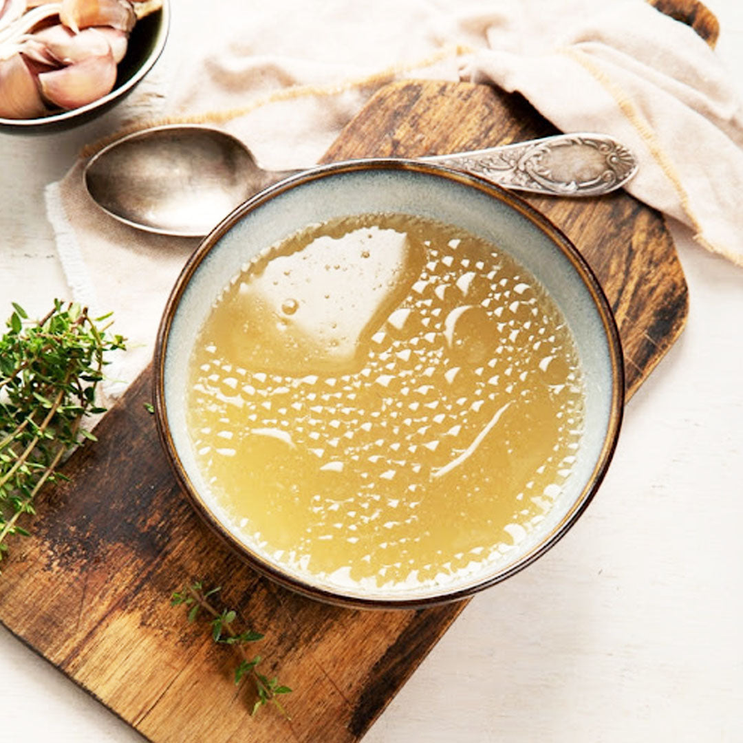Bowl of soup on a wooden cutting board with thyme and a spoon