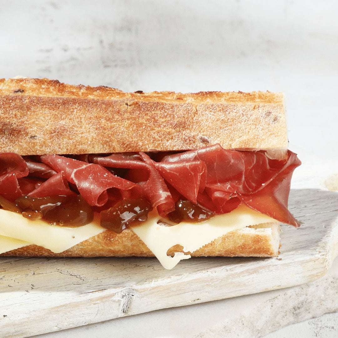 Sandwich with bresaola, cheese, and fig jam on a wooden board.