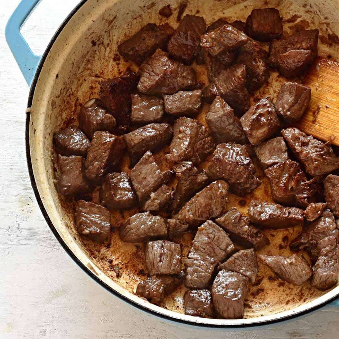 Browned beef cubes in a pan with a wooden spoon