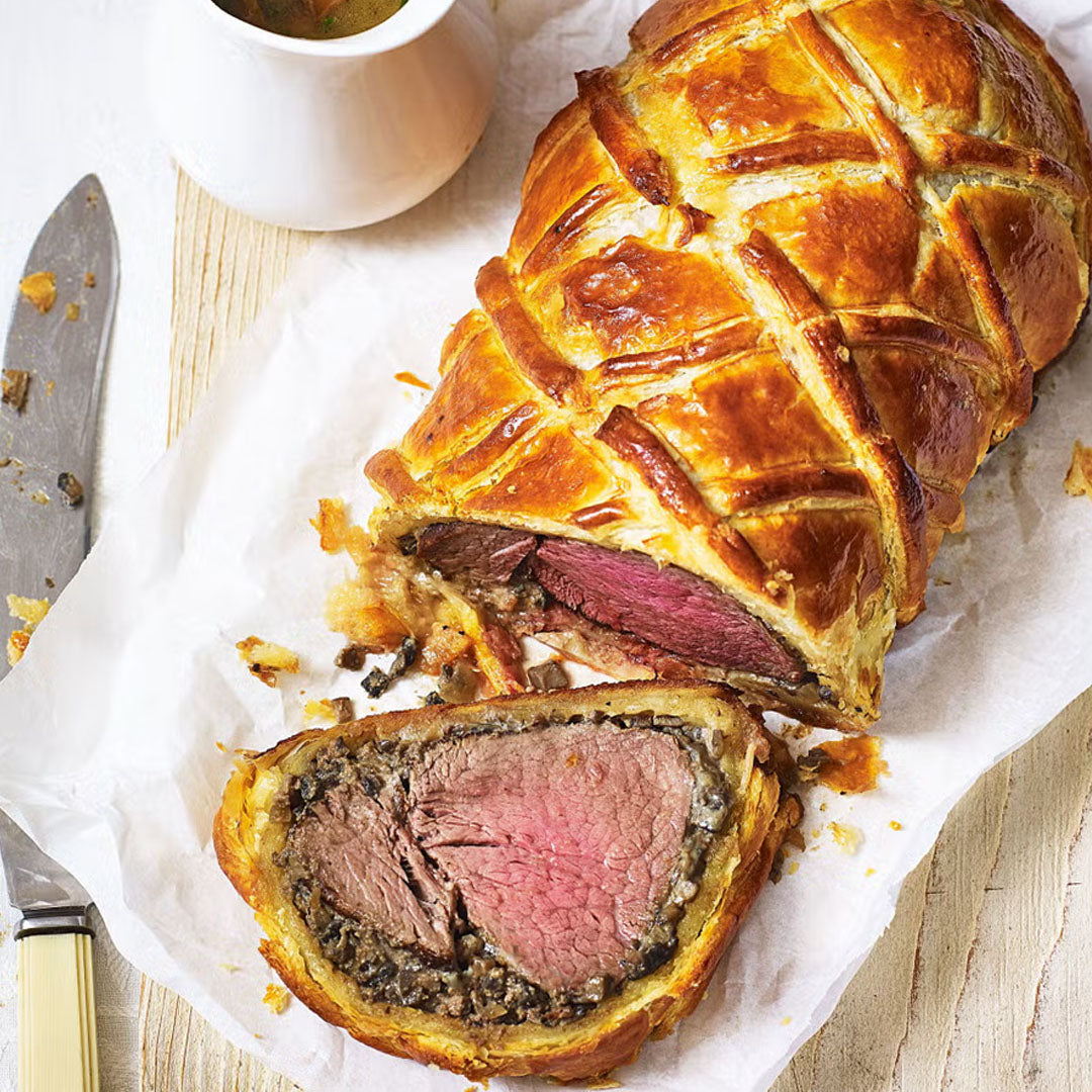  beef wellington with a slice cut, served on a wooden board