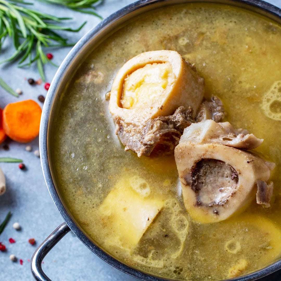 Bone broth with vegetables in a pot on a blue background