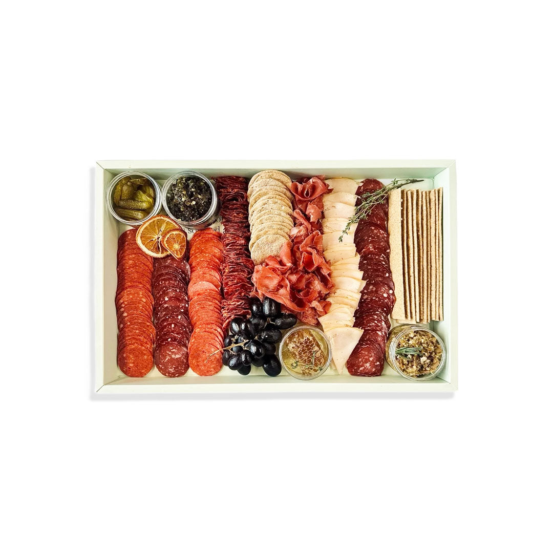 Assorted meats, cheeses, and accompaniments on a white tray with a white background