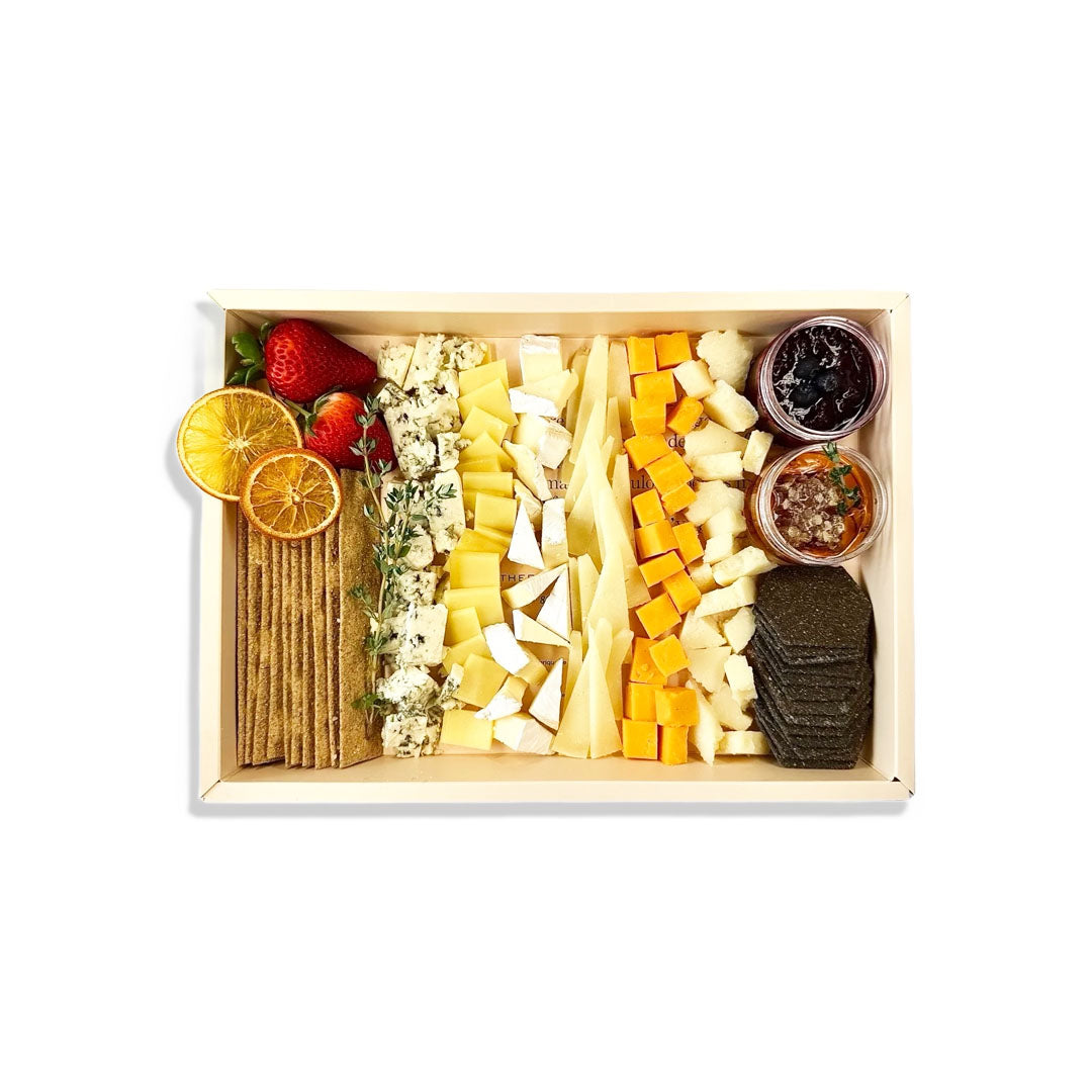 Assorted cheeses, crackers, and fruits in a wooden box on a white background