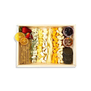 Assorted cheeses, crackers, and fruits in a wooden box on a white background
