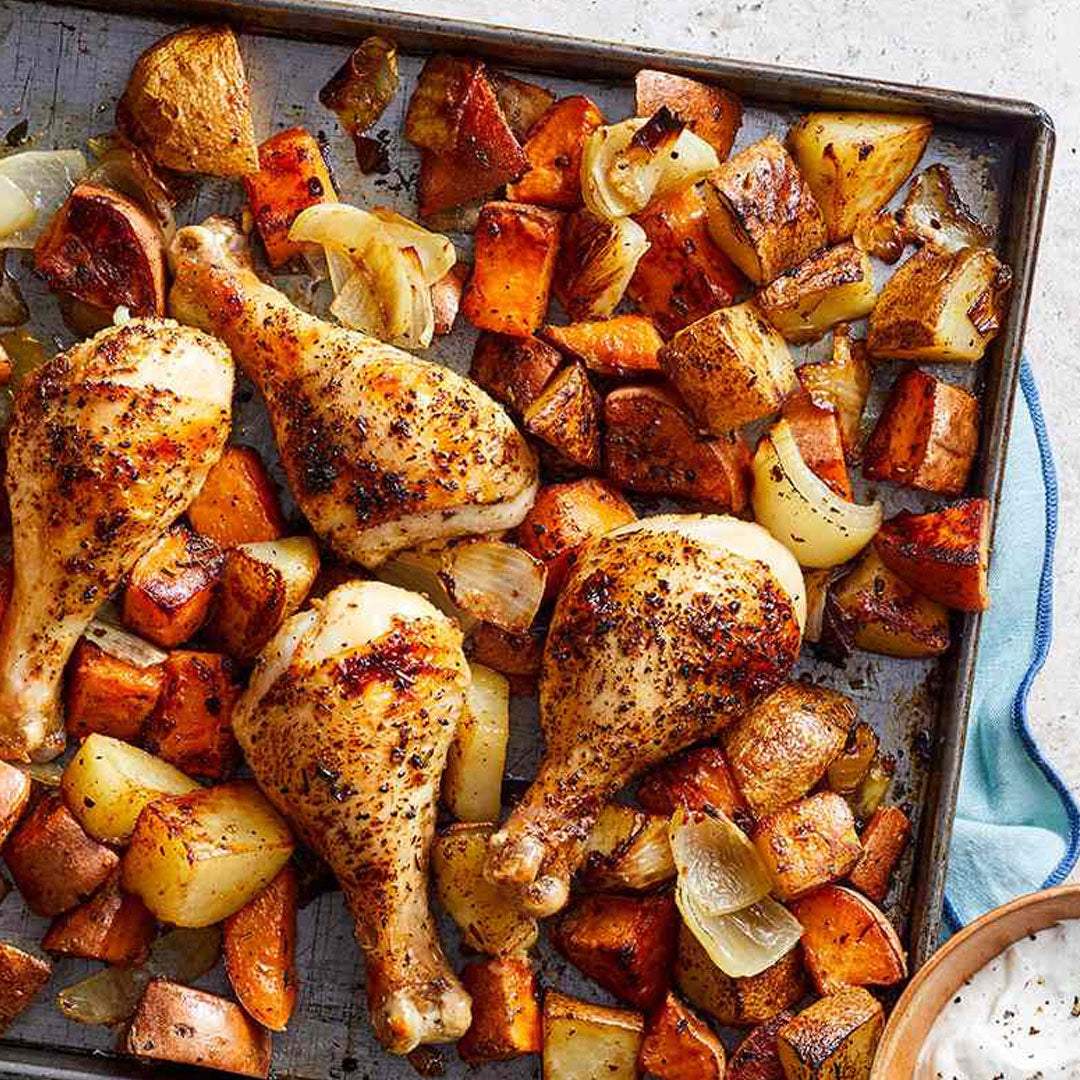 Roasted chicken drumsticks and vegetables on a baking sheet with a bowl of sauce.