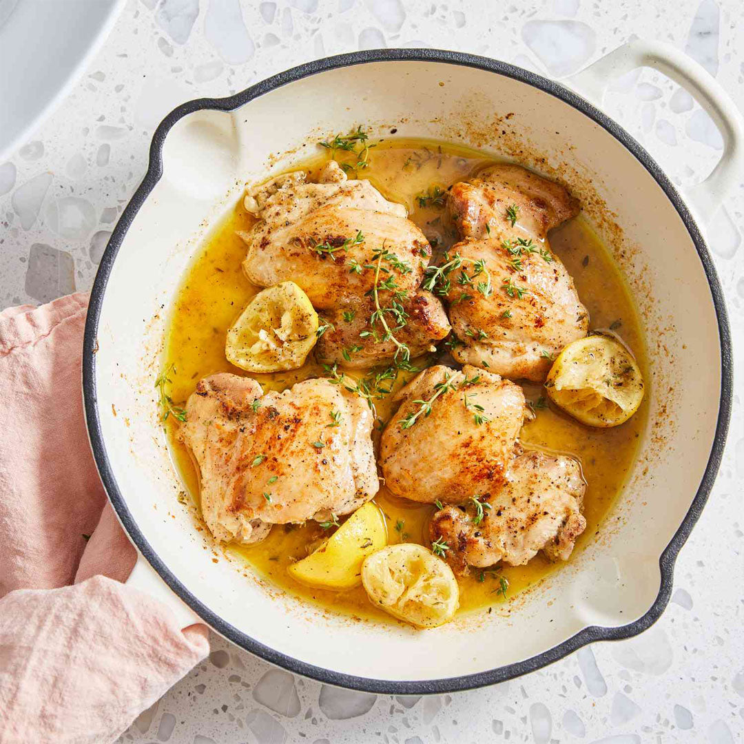 Skillet with chicken and lemon pieces on a light background