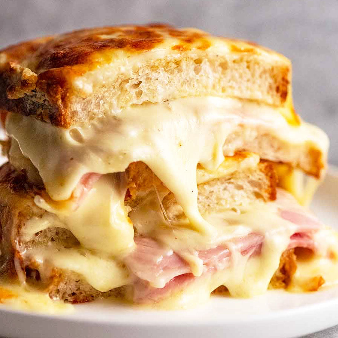 Sandwich with cheese, ham, and pickles on a plate with a blurred background