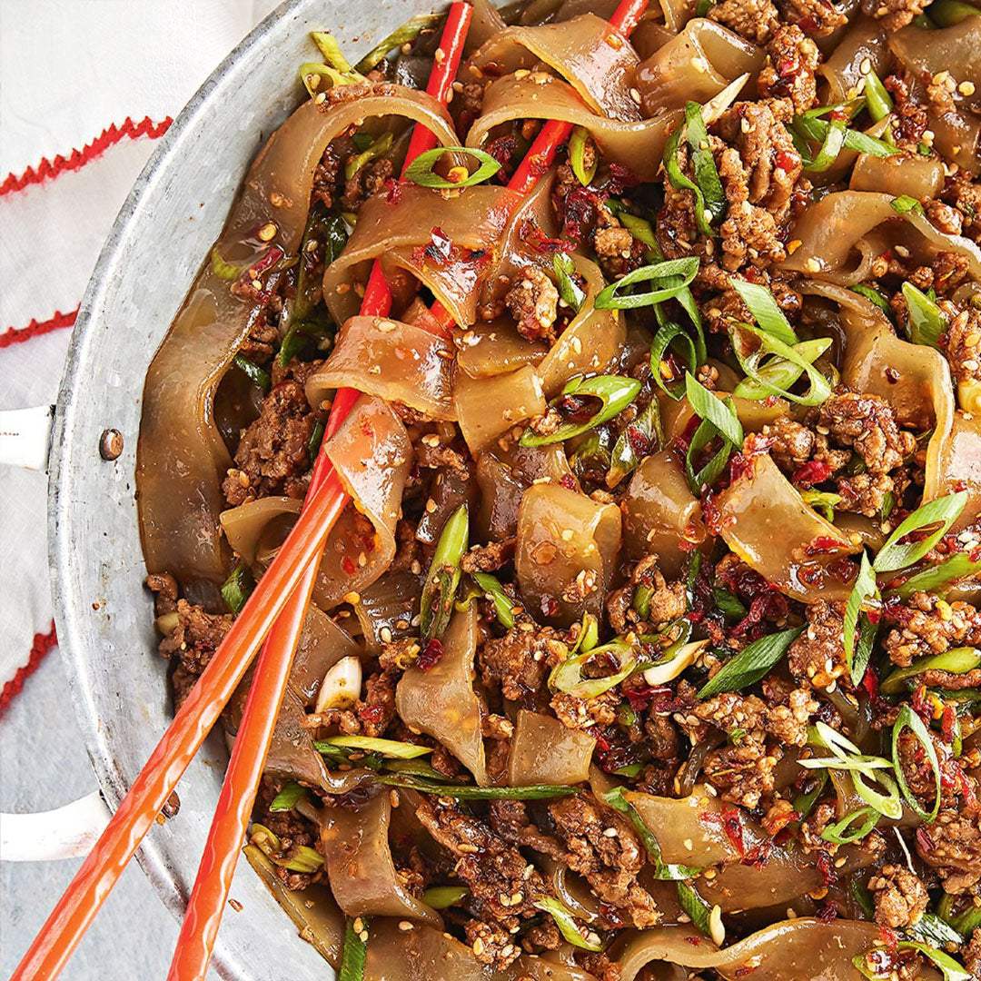 Stir-fried dish with noodles, ground meat, and vegetables in a pan with red chopsticks.