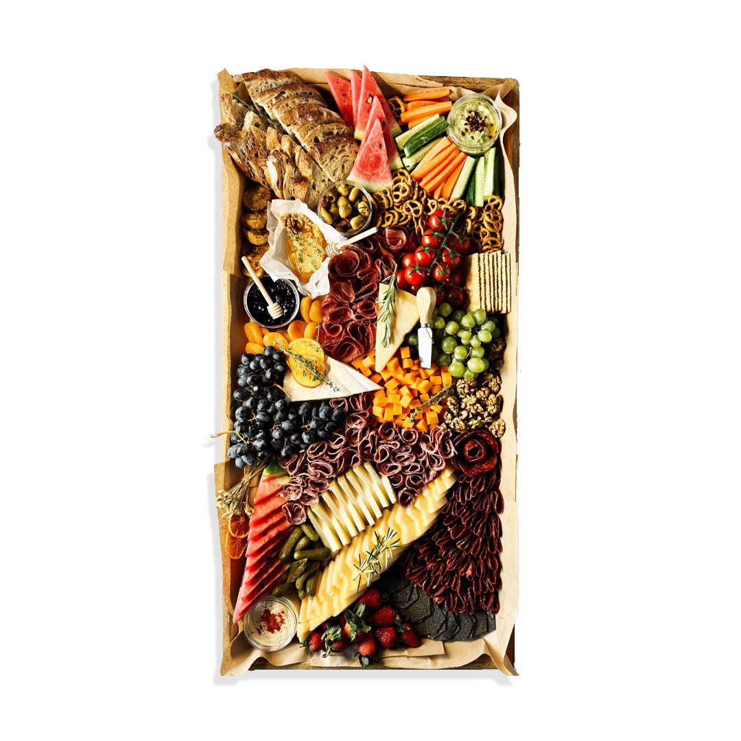 Assorted food platter with meats, cheeses, fruits, and vegetables on a white background