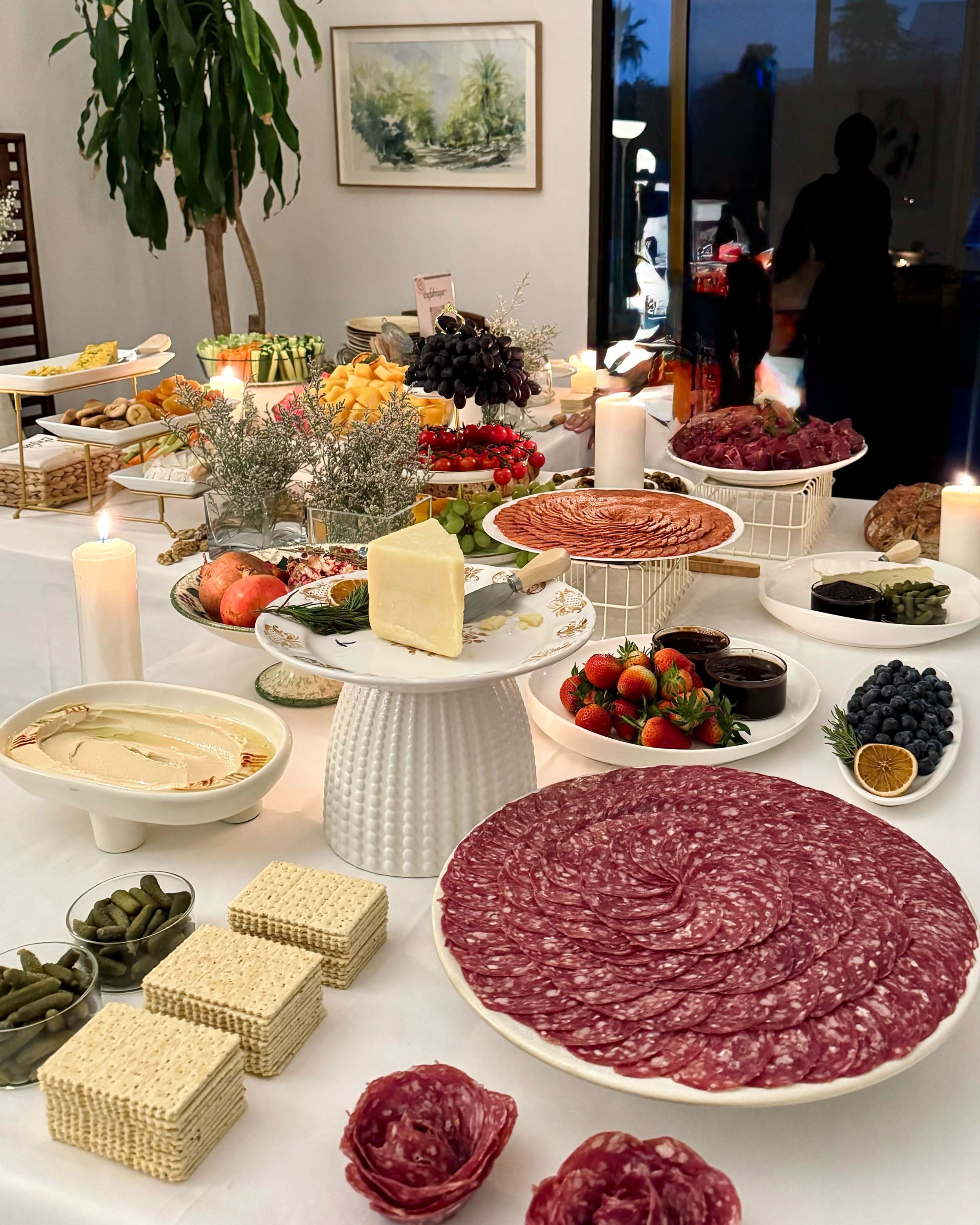 Diverse food platter with meats, cheeses, and vegetables on a table.