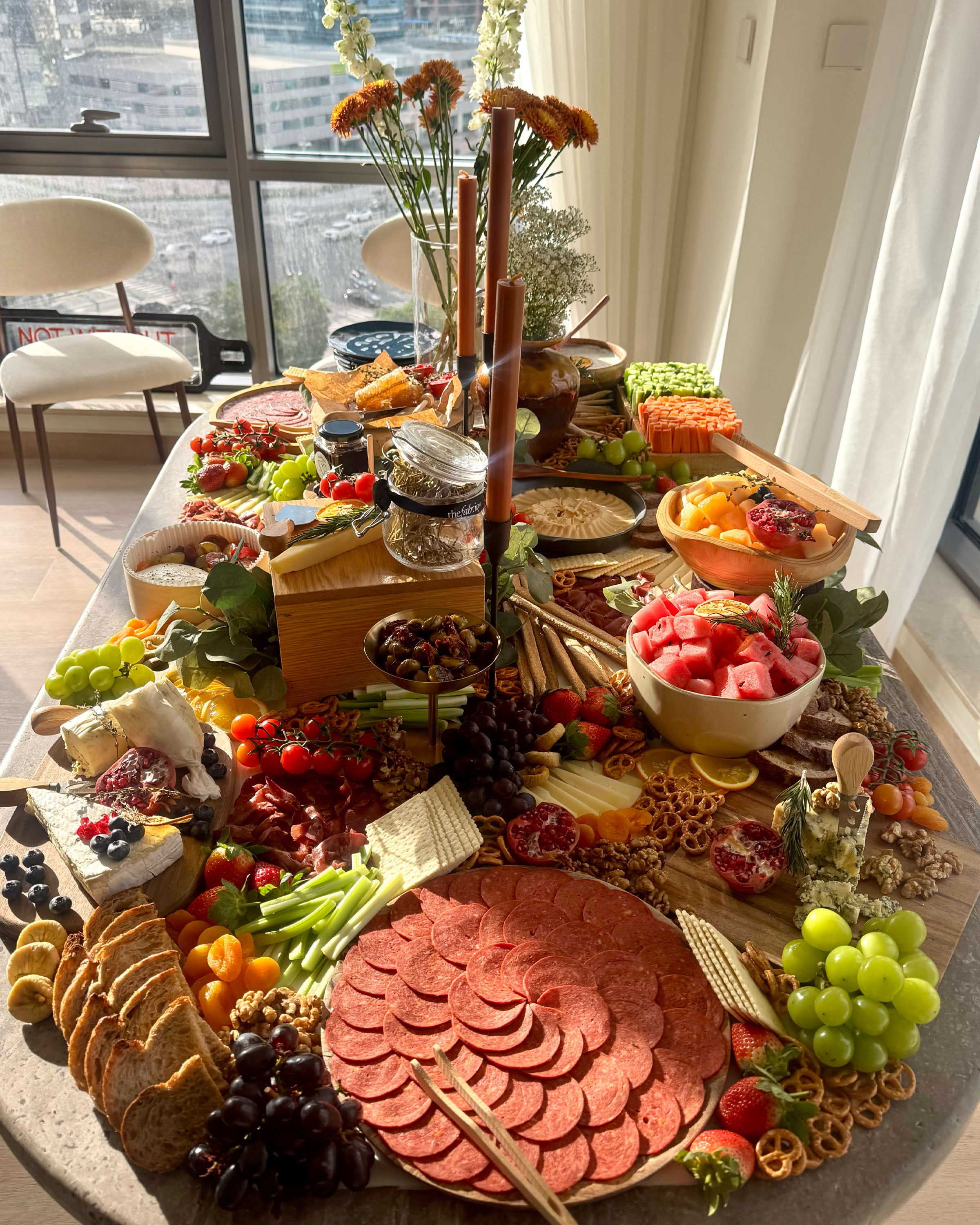 Gourmet charcuterie board with various foods on a table by a window.
