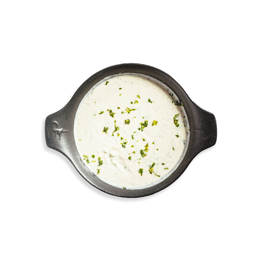 White creamy sauce with green herbs in a black bowl on a white background