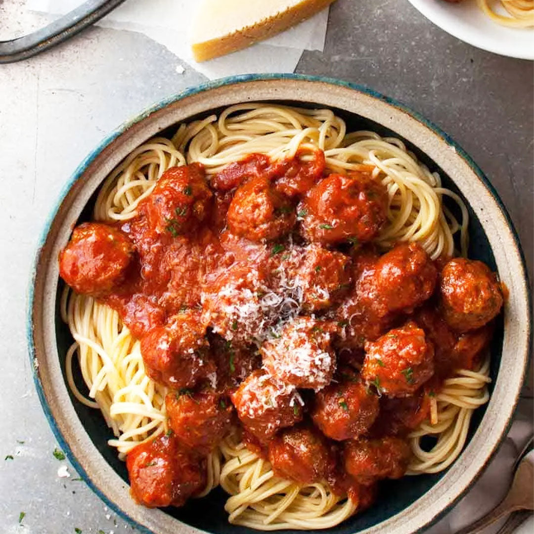 Bowl of spaghetti with meatballs on a white surface
