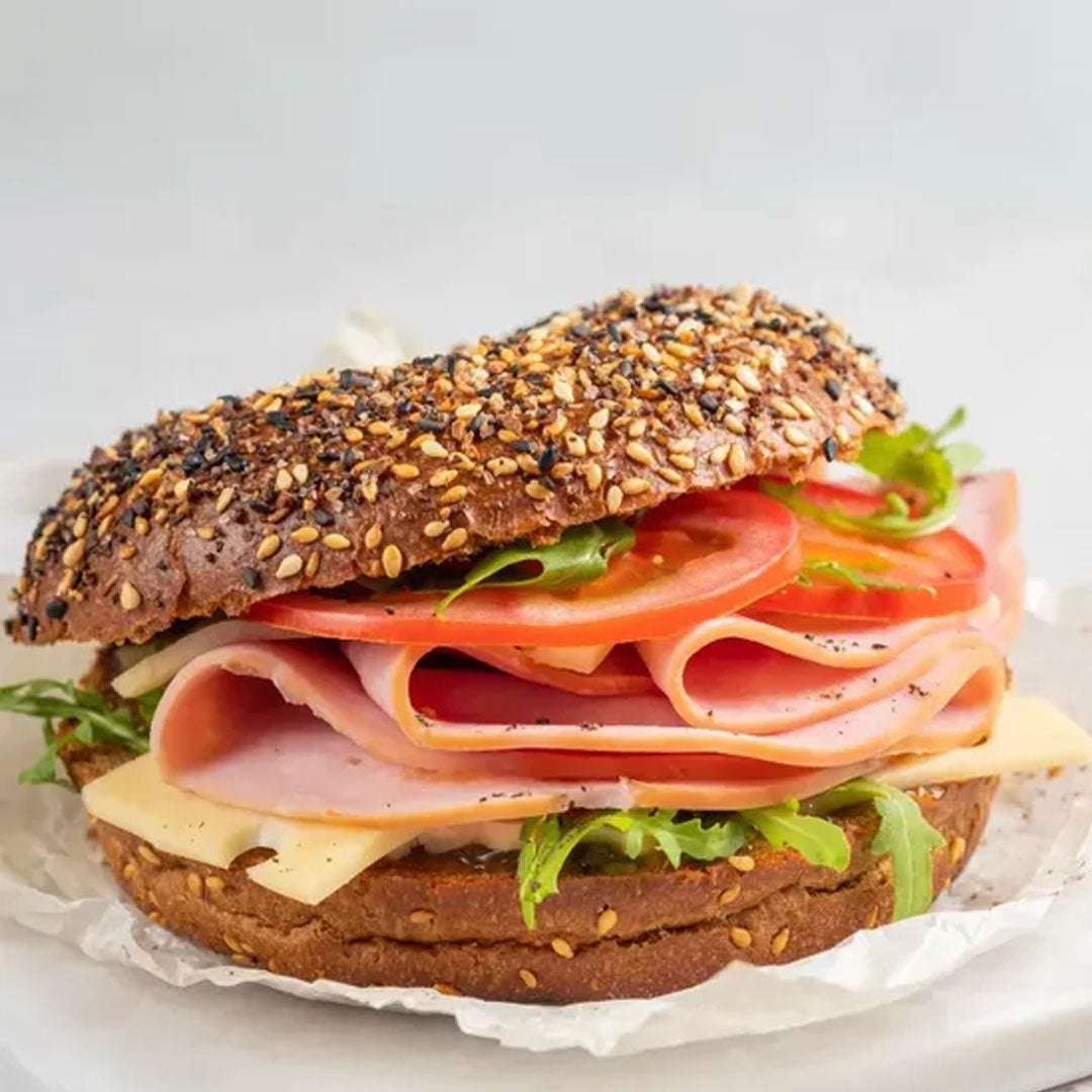 Sandwich with ham, cheese, lettuce, and tomato on a whole grain bun with sesame seeds.