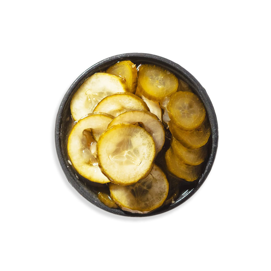 Sliced pickles in a black bowl on a white background
