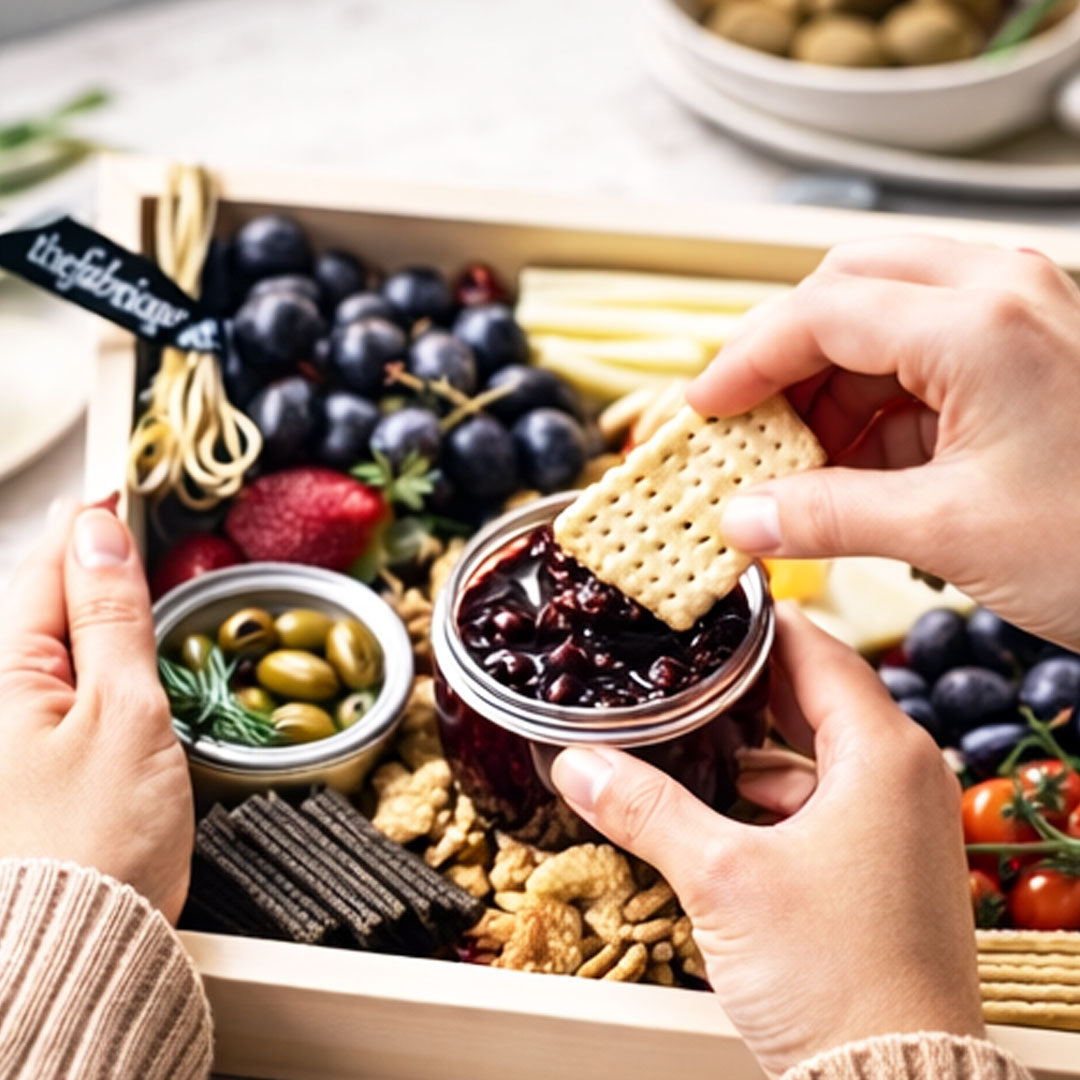 Person dipping a cracker into a jar of preserve from a charcuterie board.