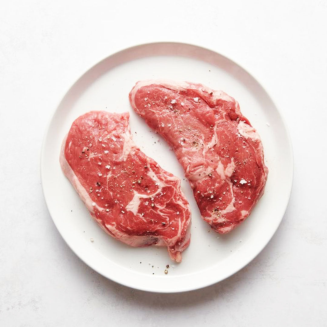 Two raw steaks on a white plate with a white background