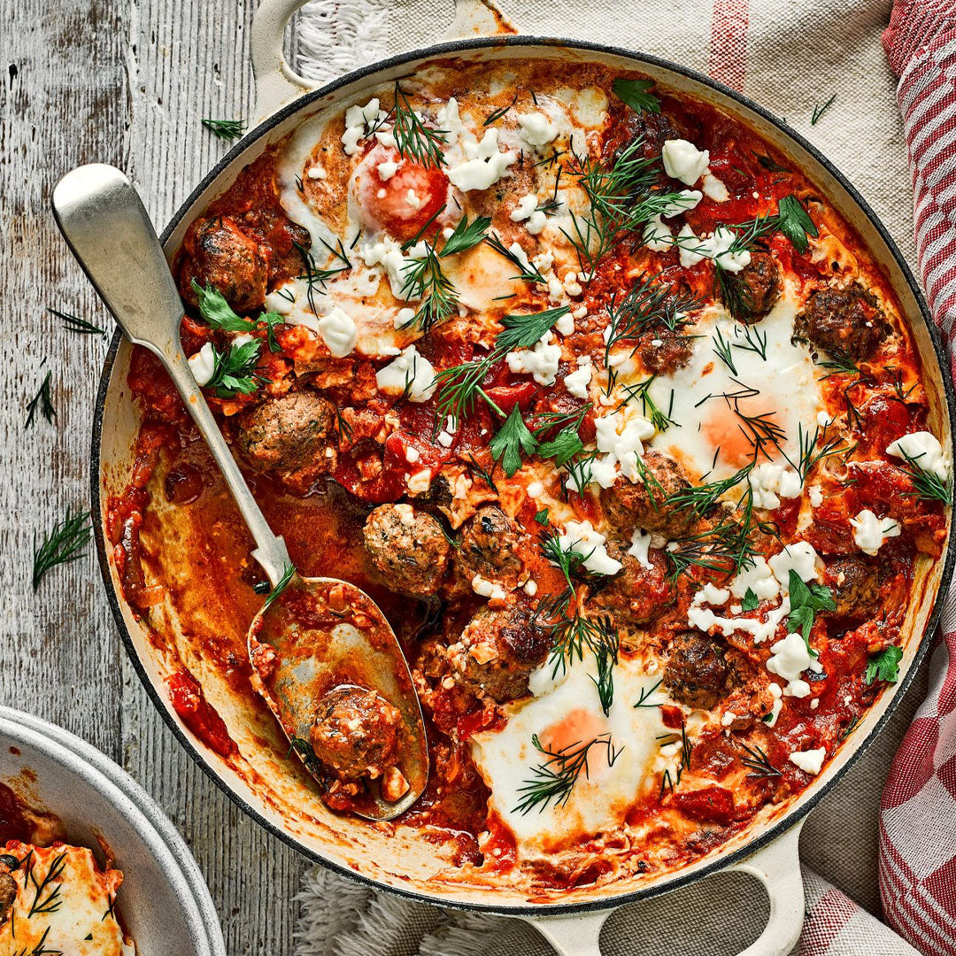 Skillet with meatballs, eggs, and herbs on a wooden table
