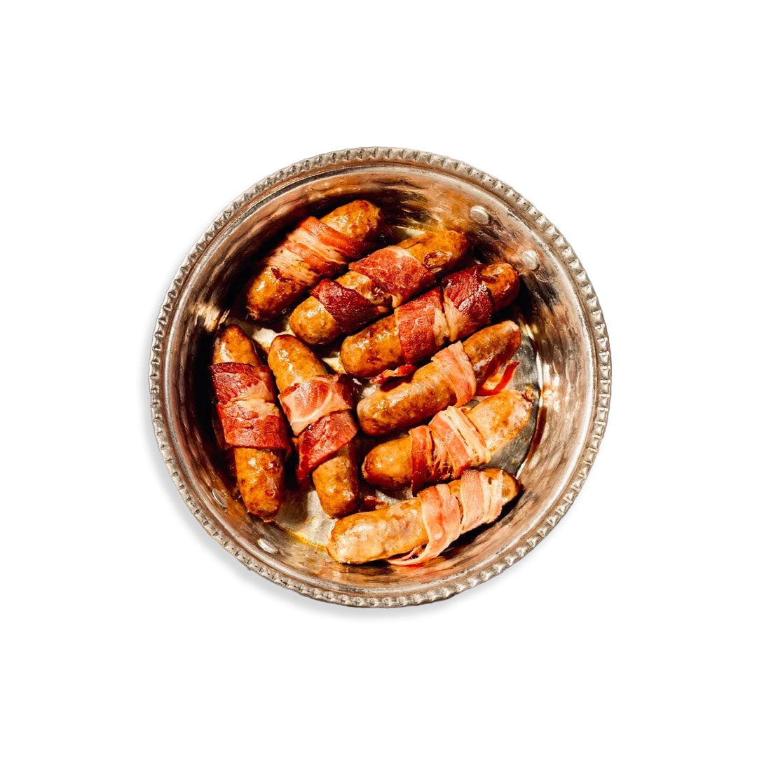 Silver bowl filled with bacon-wrapped sausages on a white background