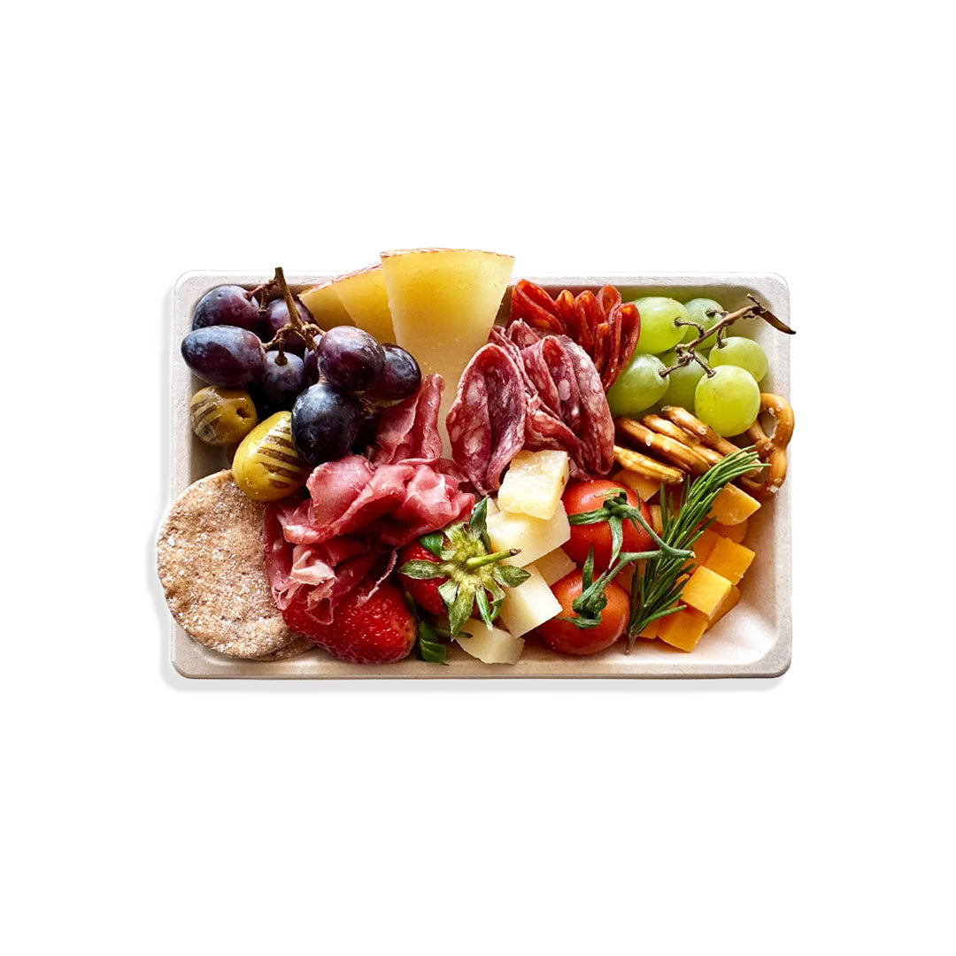 Assorted meats, cheeses, fruits, and vegetables on a white plate with a white background