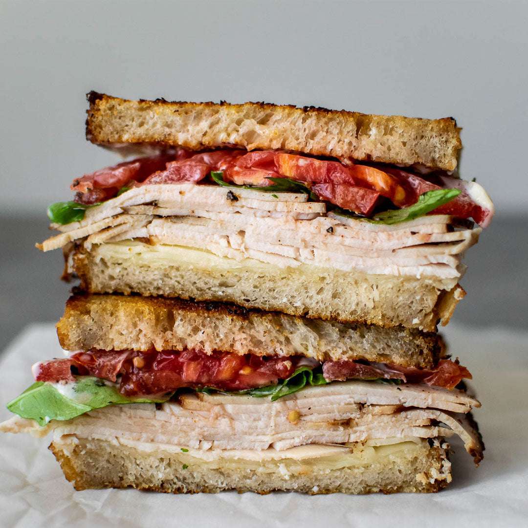 Stack of a turkey sandwich with tomato and lettuce on a gray background
