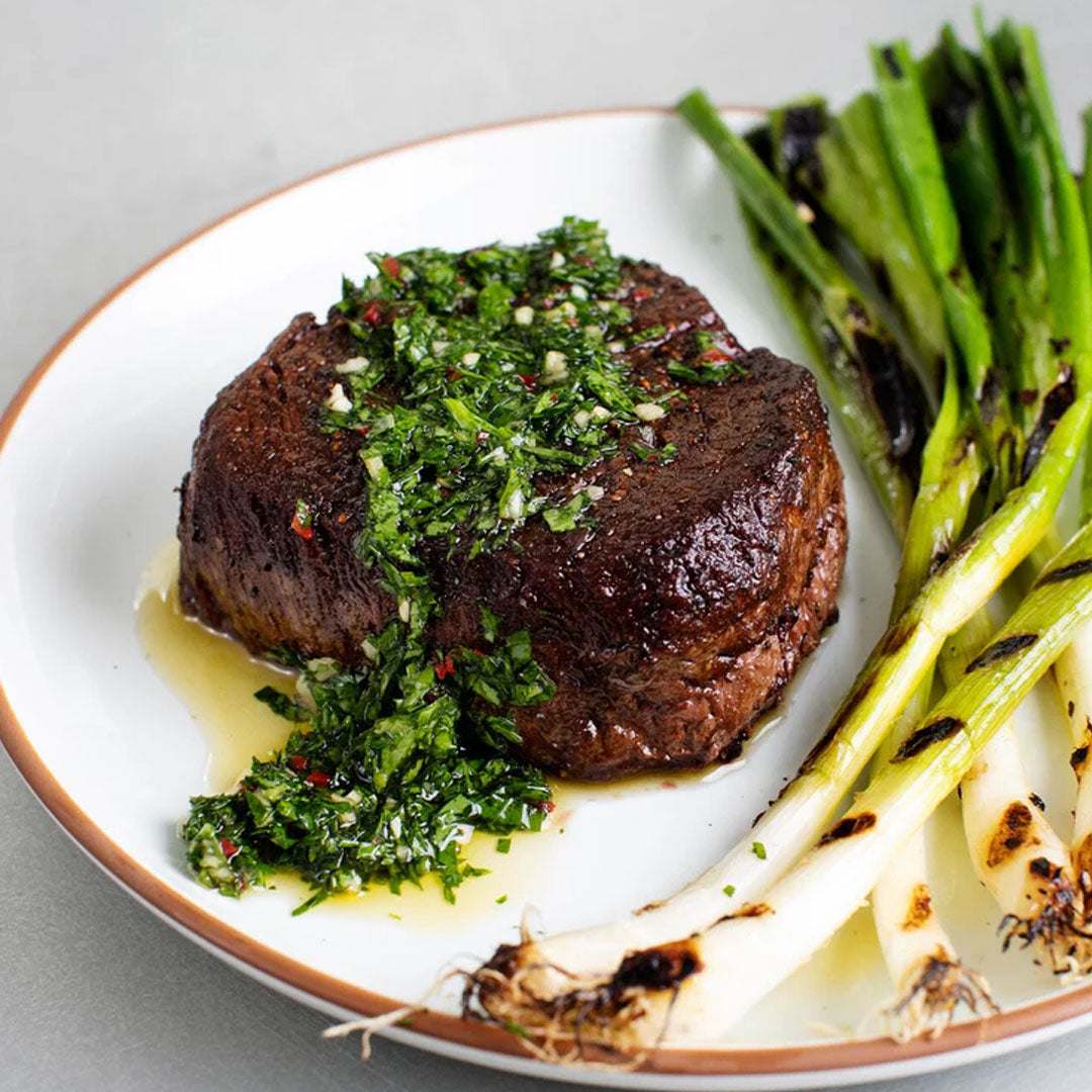 Steak with green herb sauce and grilled vegetables on a white plate