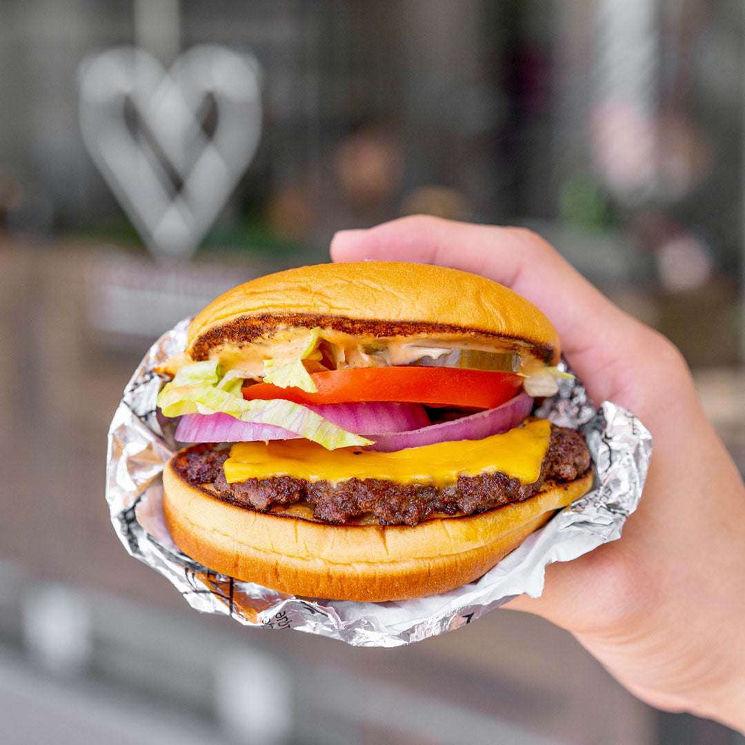 Hand holding a cheeseburger wrapped in tinfoil with a blurred background