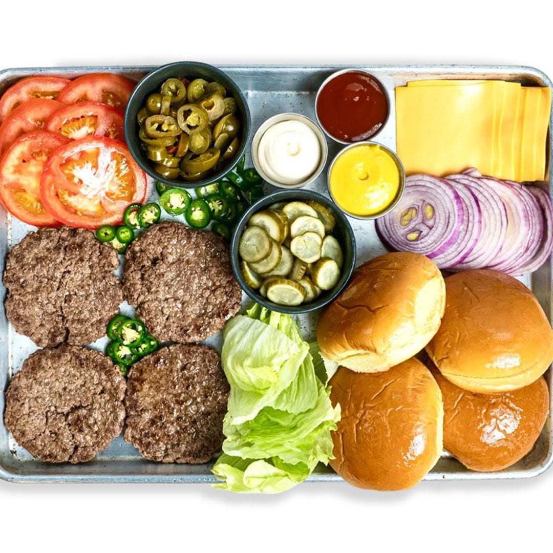 Assorted burger ingredients including buns, patties, vegetables, and condiments on a tray.