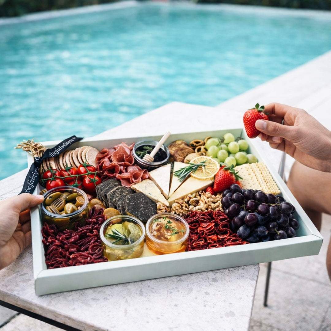 Platter of assorted foods including fruits, meats, and cheeses held by a person by a pool.