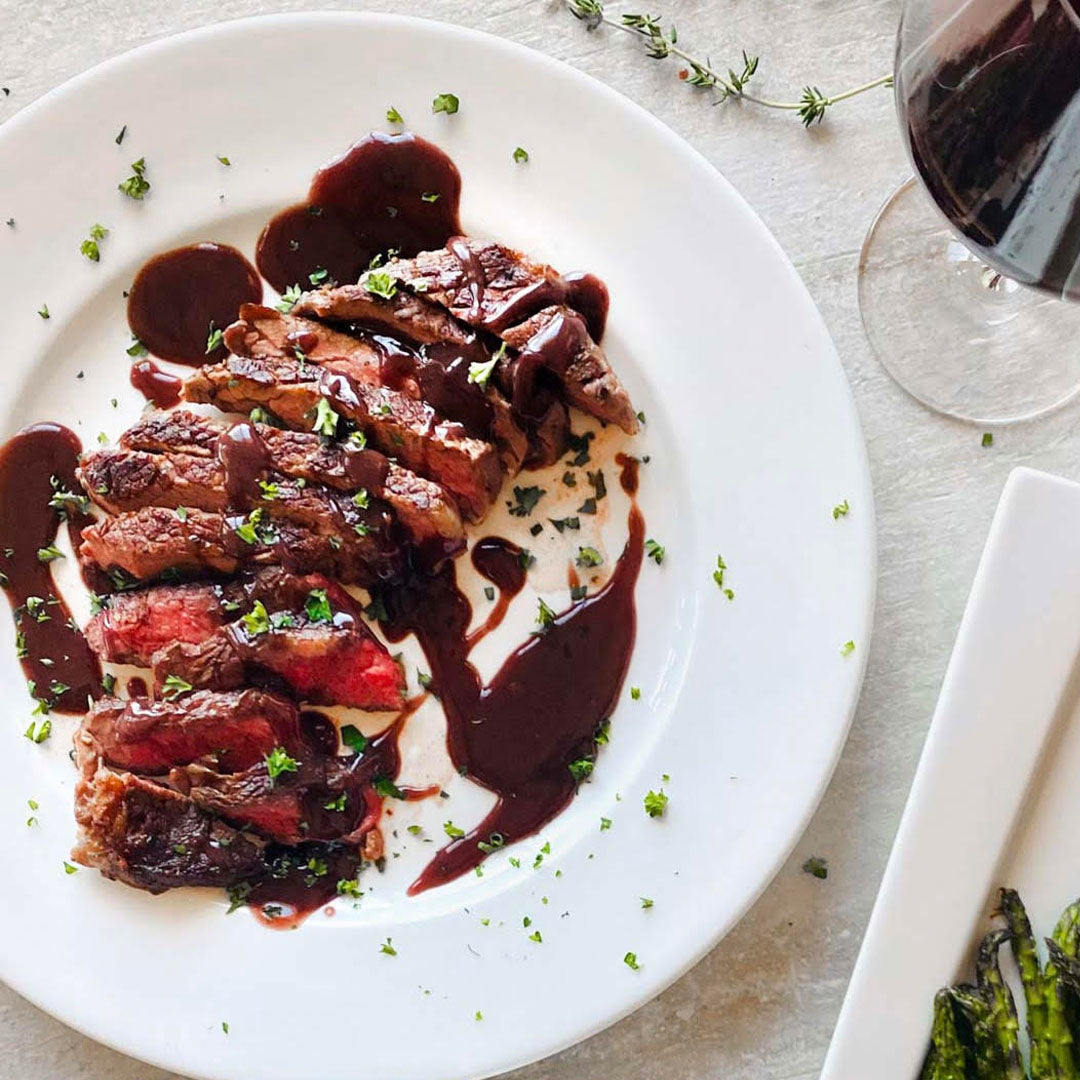 Steak with  sauce on a white plate with a glass of red wine in the background.