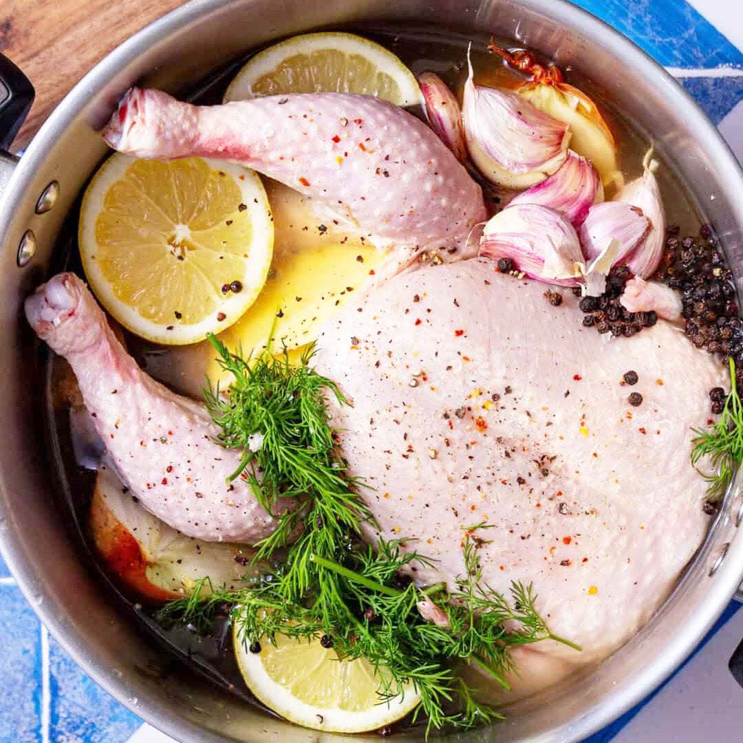 Raw chicken with lemon, garlic, and herbs in a pot on a blue surface