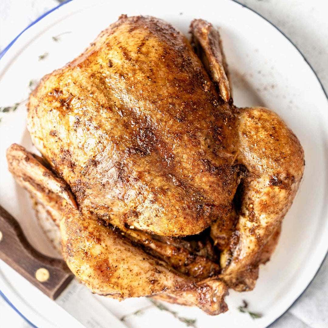 Roasted chicken on a white plate with a wooden cutting board