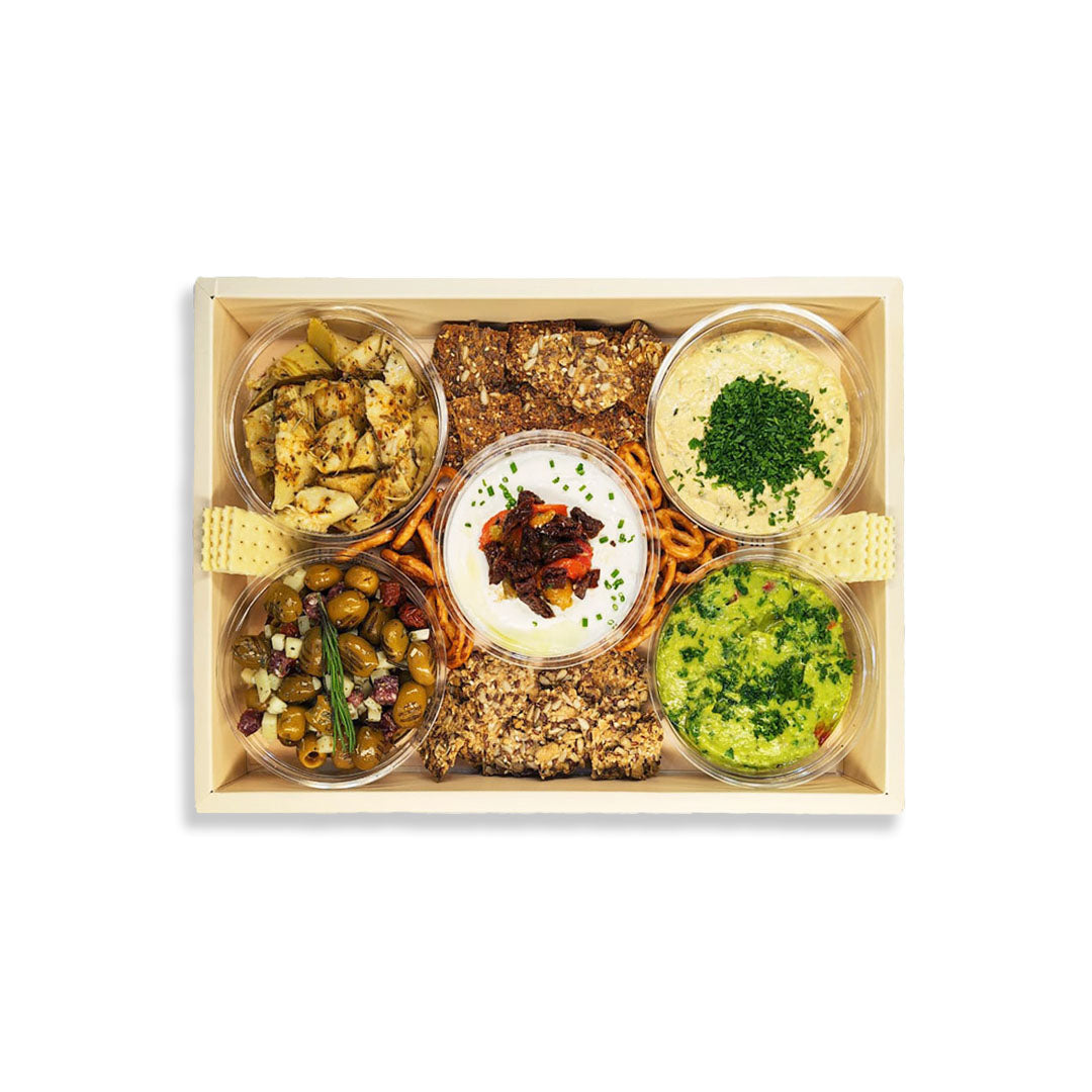 A top-down view of a Mediterranean-style food gift box in a light wood tray, containing six clear plastic cups with hummus, olives, grilled fish, and flatbread, arranged neatly on a white background.