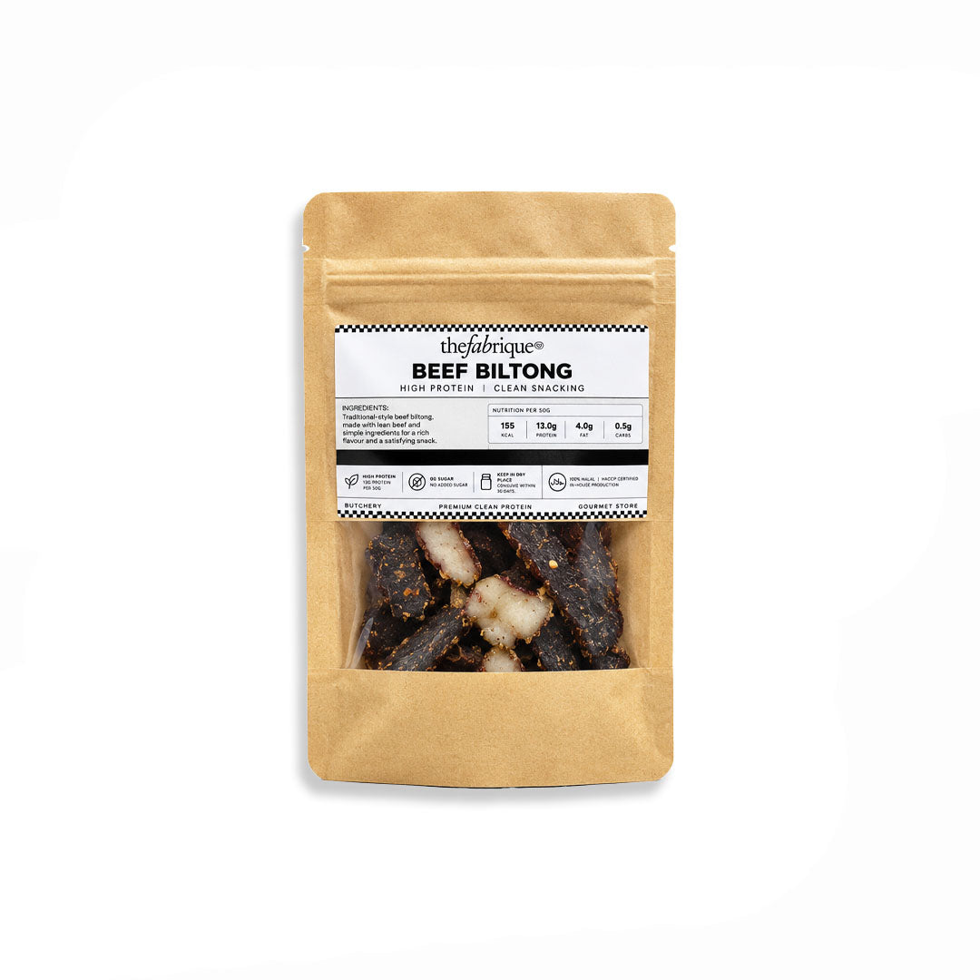 A kraft paper stand-up pouch of 'thefabrikke' Beef Biltong with a clear window showing the dark cured meat inside, set against a plain white background.