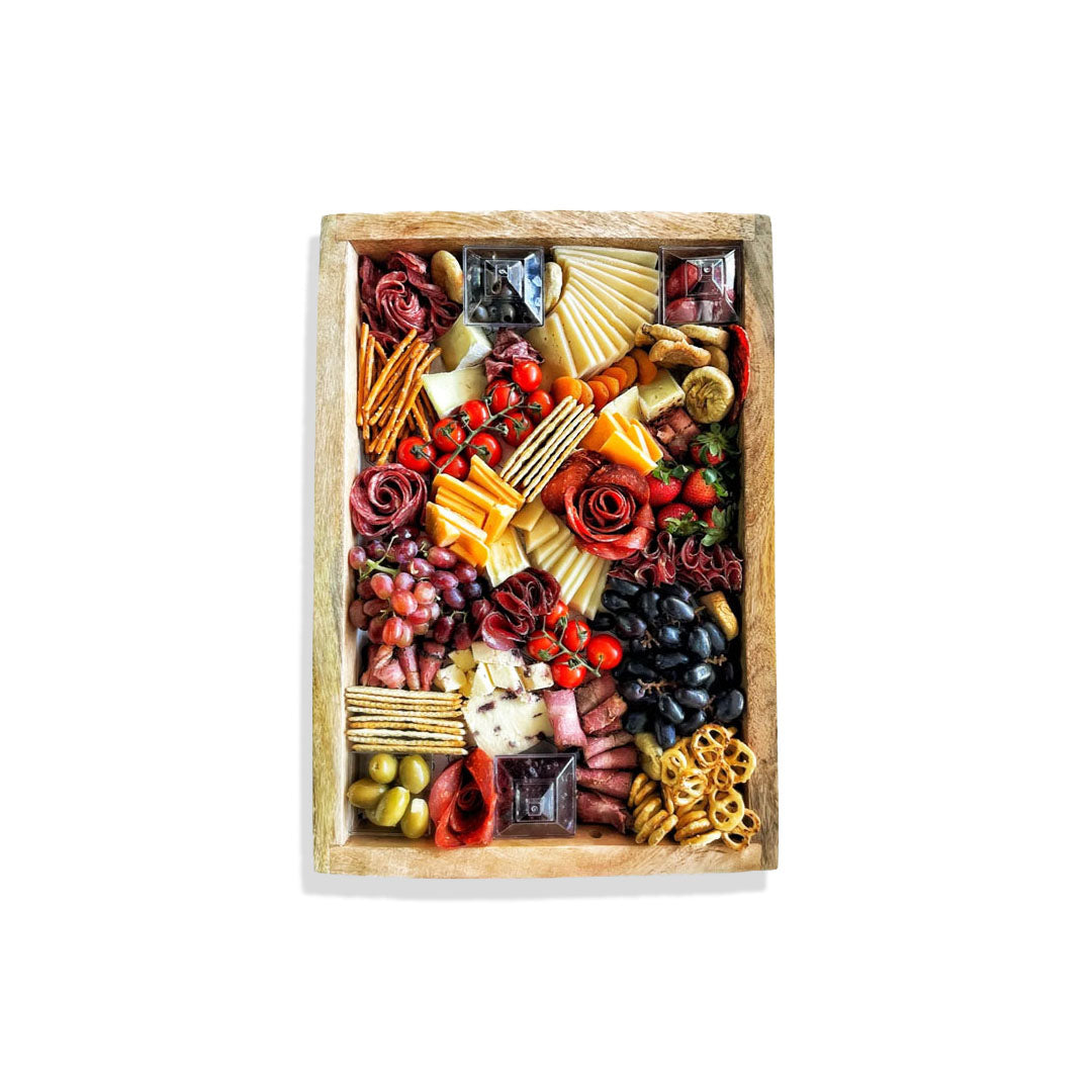 Wooden charcuterie board with a variety of meats, cheeses, fruits, and vegetables on a white background