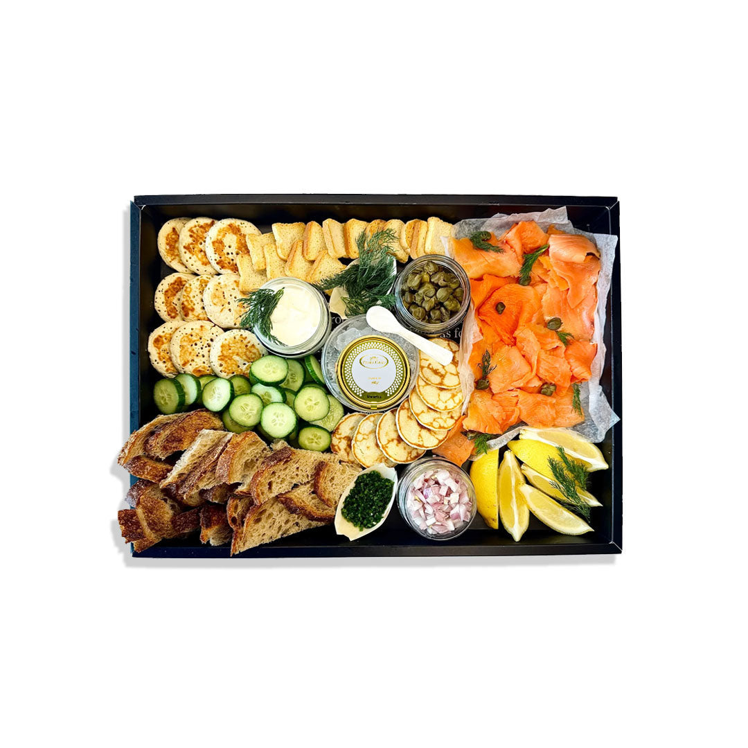 Assorted food platter with salmon, crackers, and vegetables on a white background