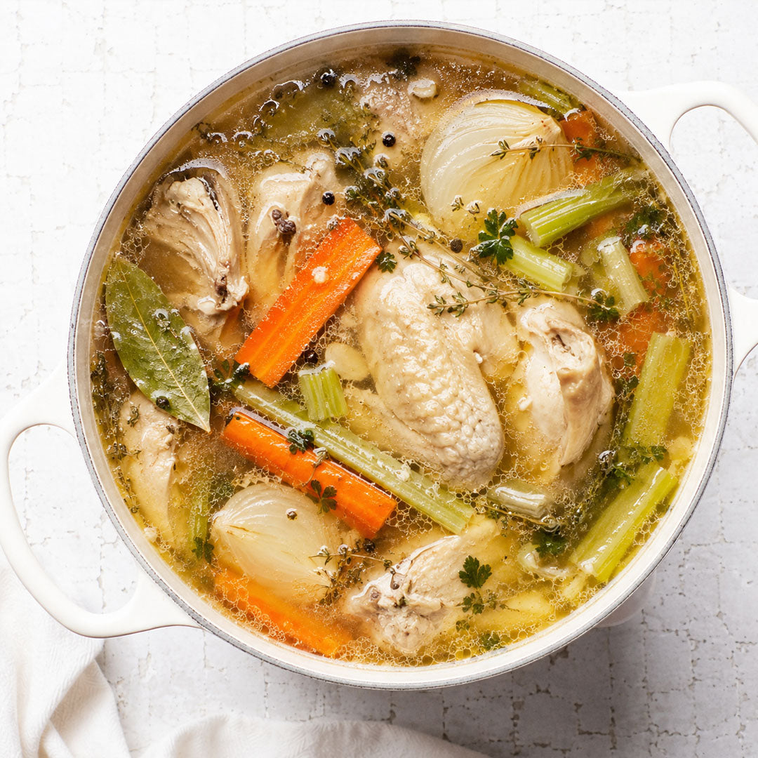 Pot of chicken soup with vegetables on a light background