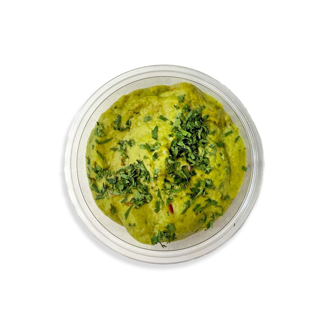 Green hummus with herbs in a clear container on a white background