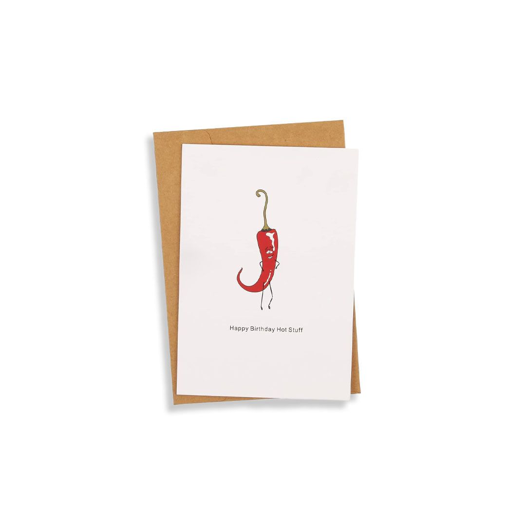 A white greeting card with a red chili pepper illustration and the text 'Happy Birthday Hot Shot' is shown with a brown kraft envelope on a clean white background.