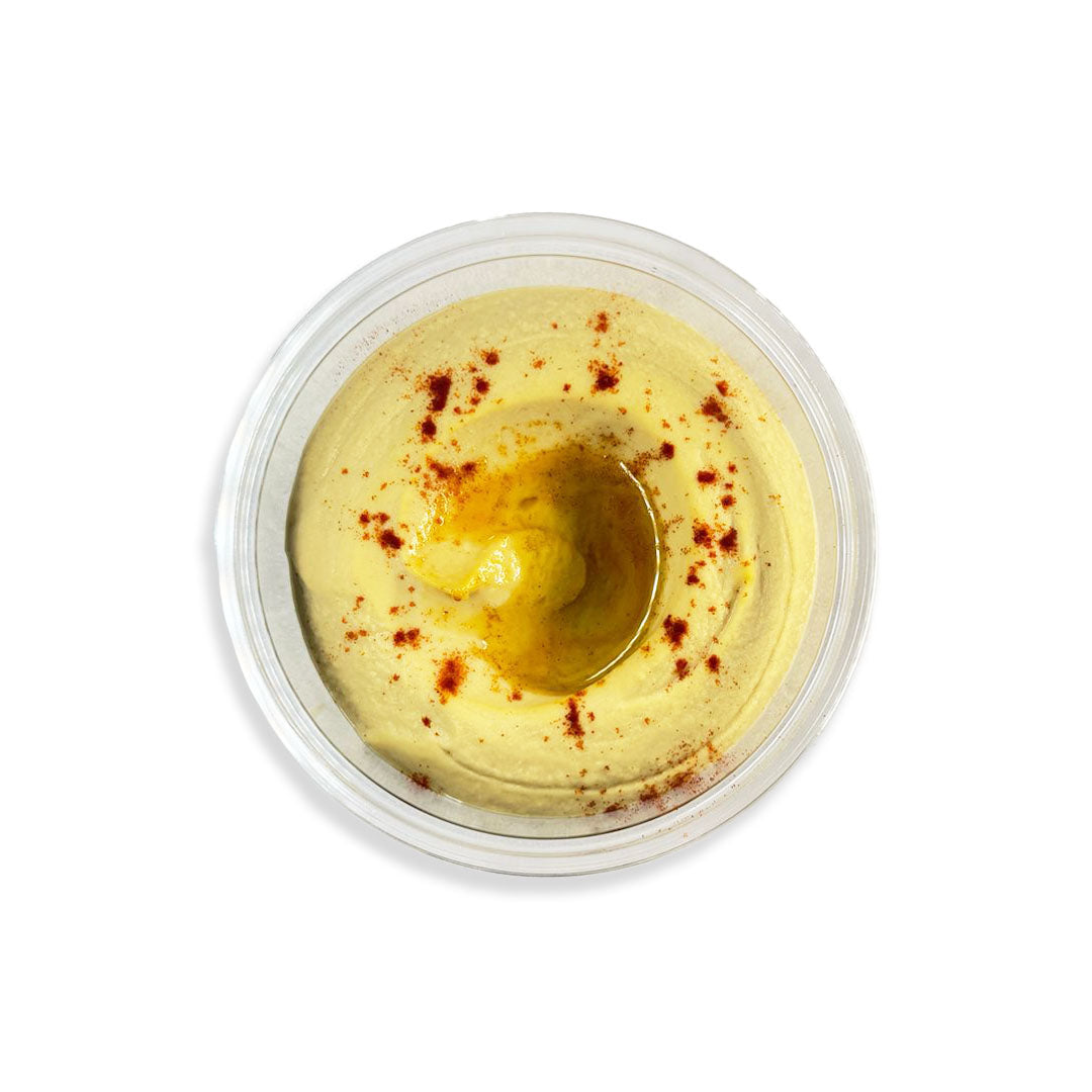 Yellow hummus in a clear plastic container on a white background