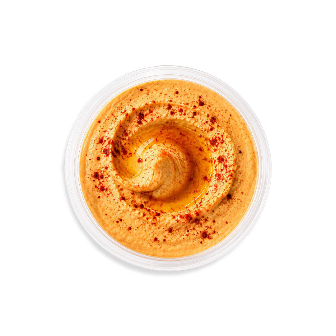 paprika hummus in a plastic container on a white background