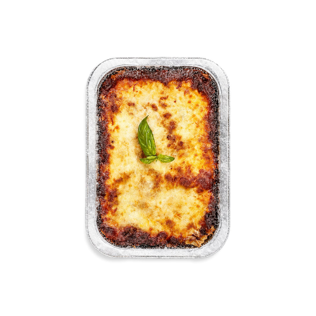 Lasagna in a rectangular container with a basil leaf on a white background