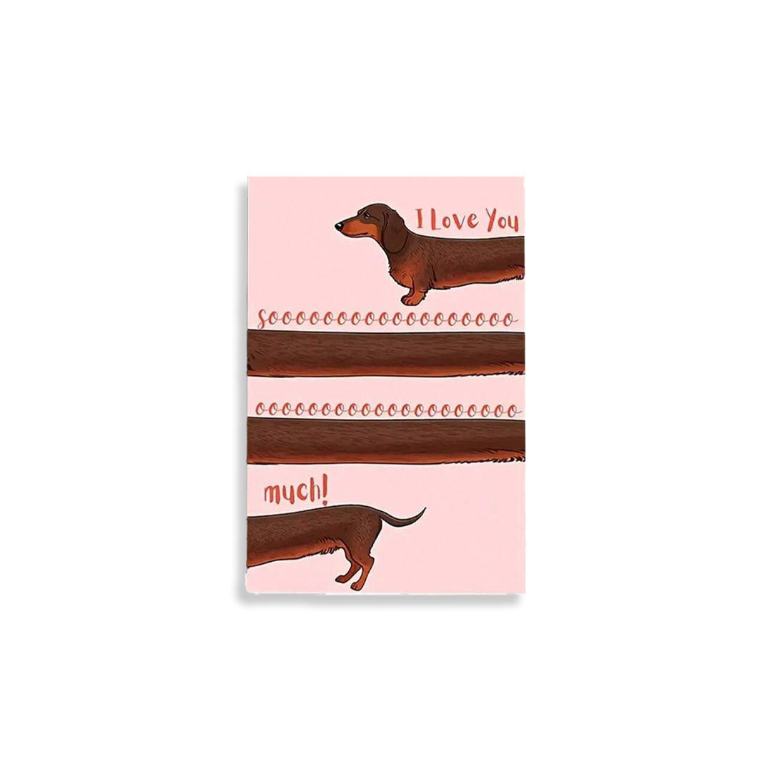 A rectangular pink card or print featuring illustrated dachshund dogs and the words 'I love you' and 'much!' on a white background.