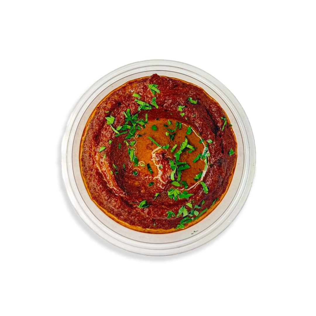 Red hummus with green herbs in a clear container on a white background