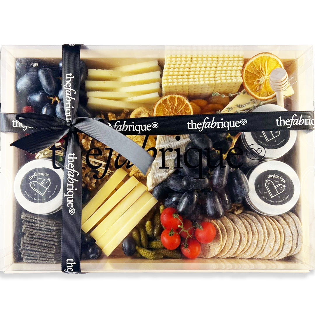 Gourmet food gift set with cheeses, fruits, and crackers in a box, branded 'thefabrique'.